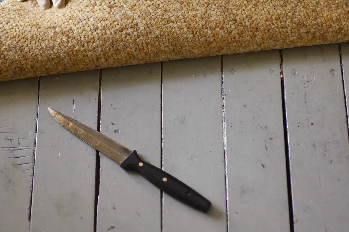 Oud tapijt dat wordt opgerold met de lichte rug naar boven, op geschilderde grijze houten planken met een mes ernaast